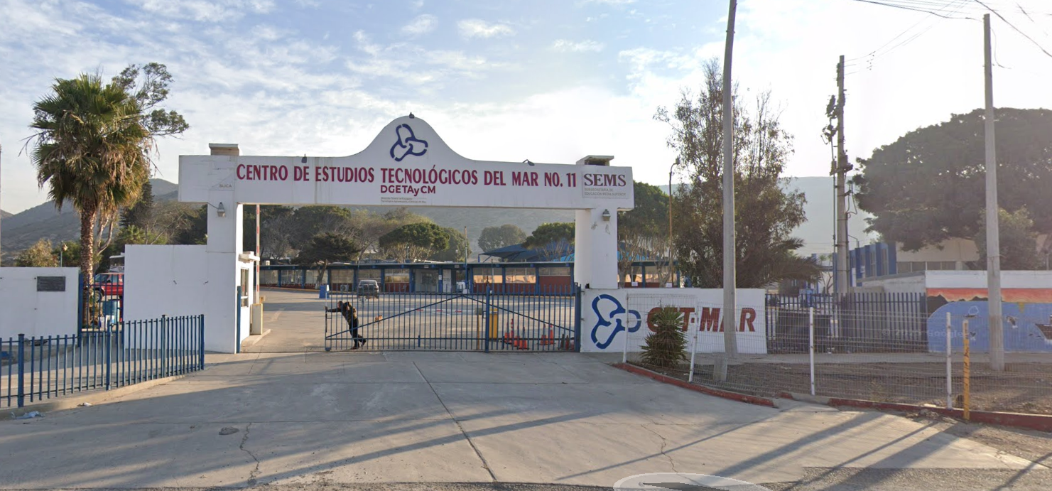 Se muestra la entrada del plantel conformada por un arco color blanco y una reja color azul, sobre el arco en letras grandes dice CENTRO DE ESTUDIOS TECNOLÓGICOS DEL MAR NÚMERO 11. 
